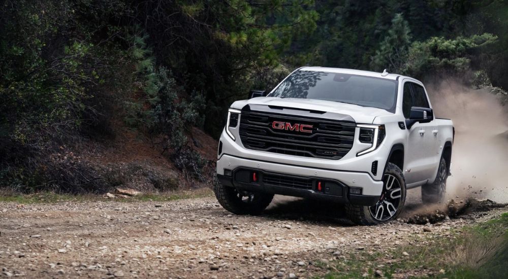 A white 2024 GMC Sierra 1500 AT4 is shown kicking up dust after leaving a GMC dealer near Owosso.