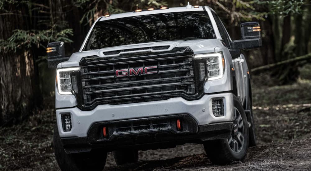 A white 2024 GMC Sierra 2500 HD AT4 is shown from a front angle while driving off-road.
