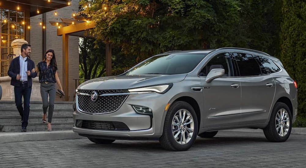 Two people walking towards a grey 2024 Buick Enclave parked beside a curb.