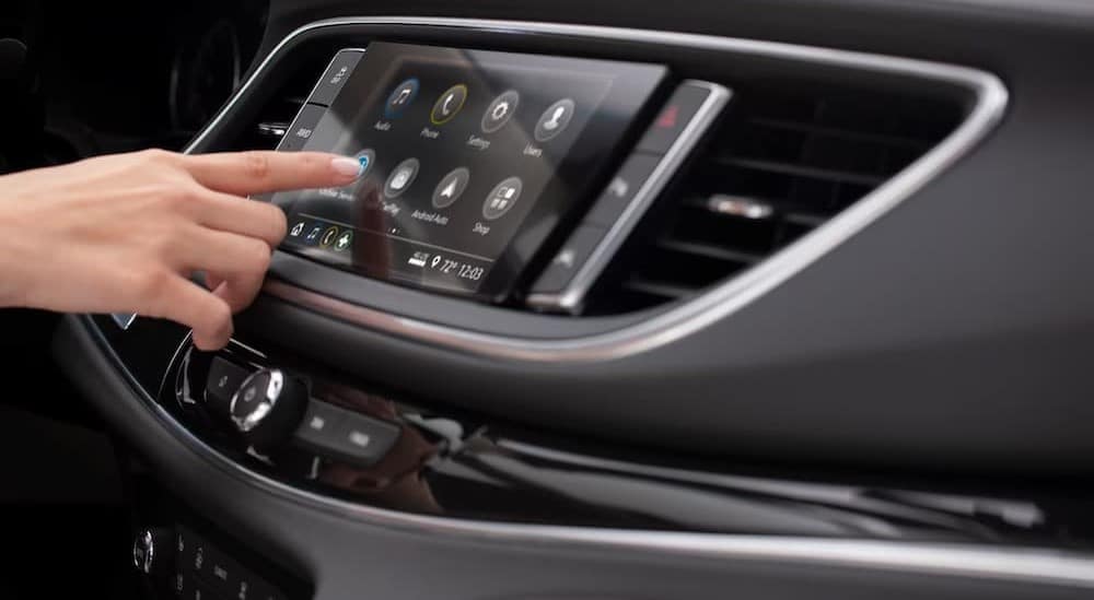 A hand pressing on the infotainment dashboard in the black interior of a 2024 Buick Enclave.