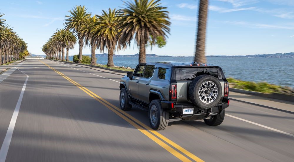 Rear angle view of a silver 2024 GMC Hummer EV driving by the ocean.