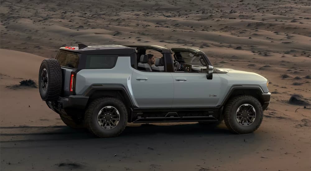 Side angle view of a white 2024 GMC Hummer EV parked on a sand dune.