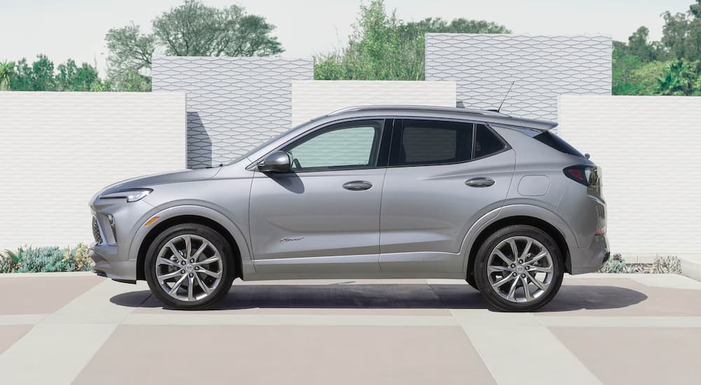 Side angle view of a silver 2025 Buick Encore GX parked by a brick wall.