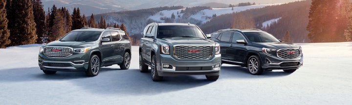 A trio of grey GMC vehicles parked in a snowy field.
