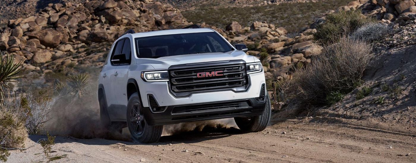White 2022 GMC Acadia driving off-road up a hill.