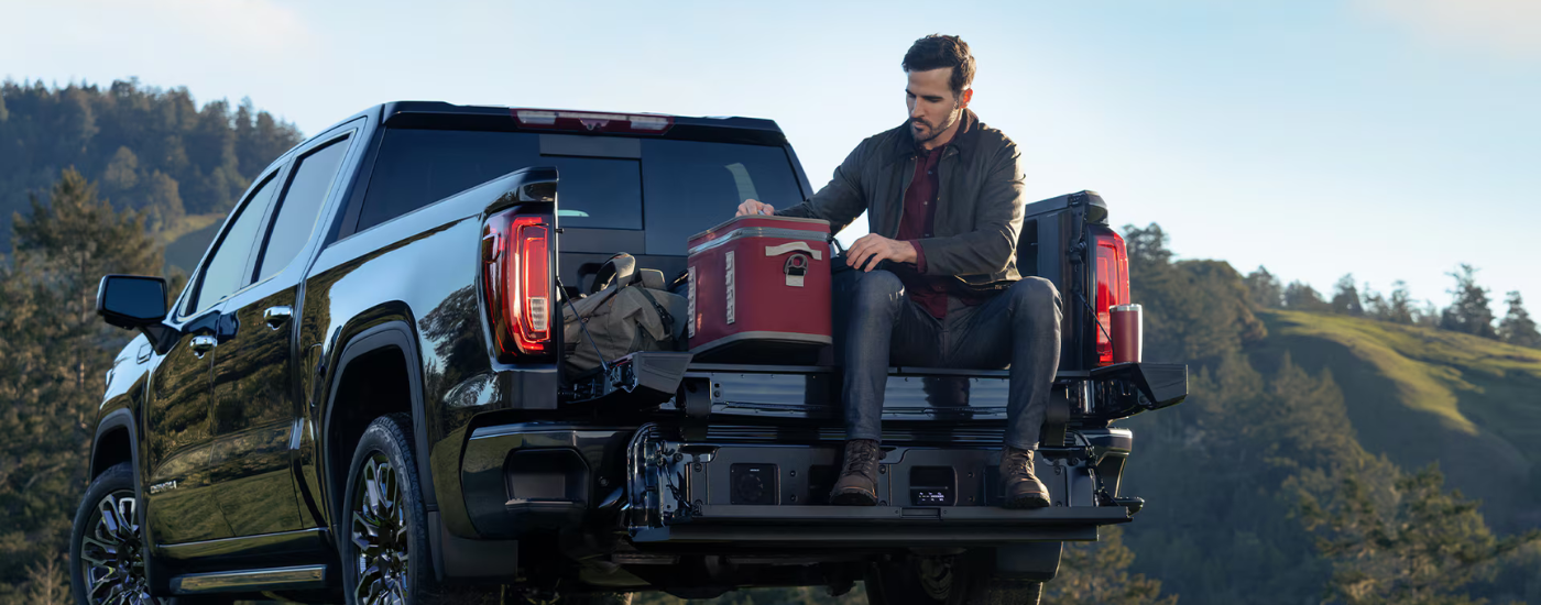 A person sitting on the tailgate of a black 2026 GMC Sierra 1500