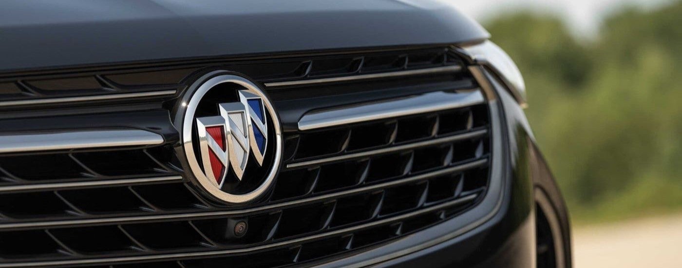 A close-up view of the Buick badge on the grille of a black 2023 Buick Envision ST is shown.