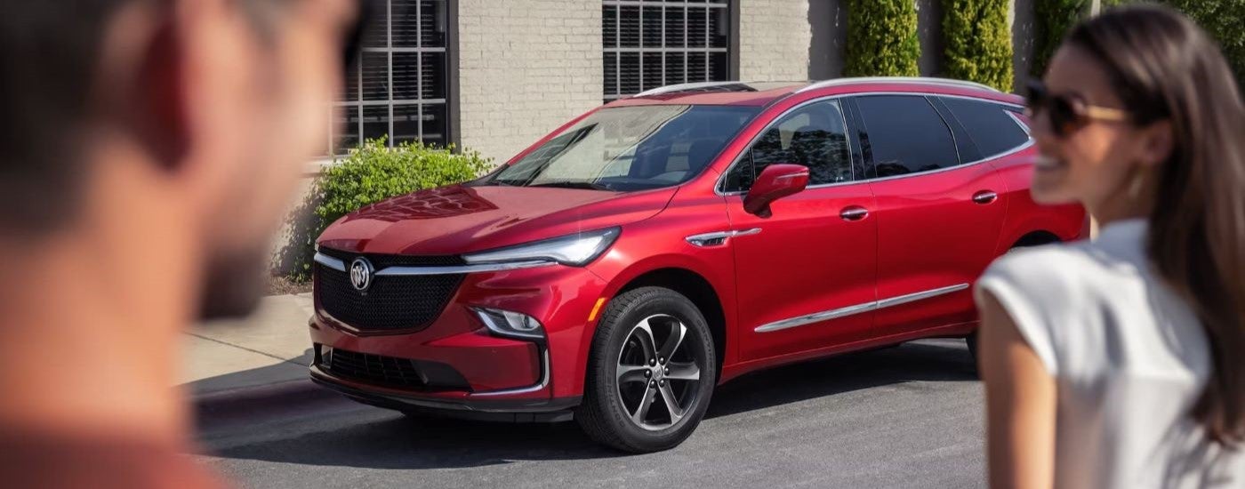 Two people walking towards a red 2024 Buick Enclave ST parked by a curb.