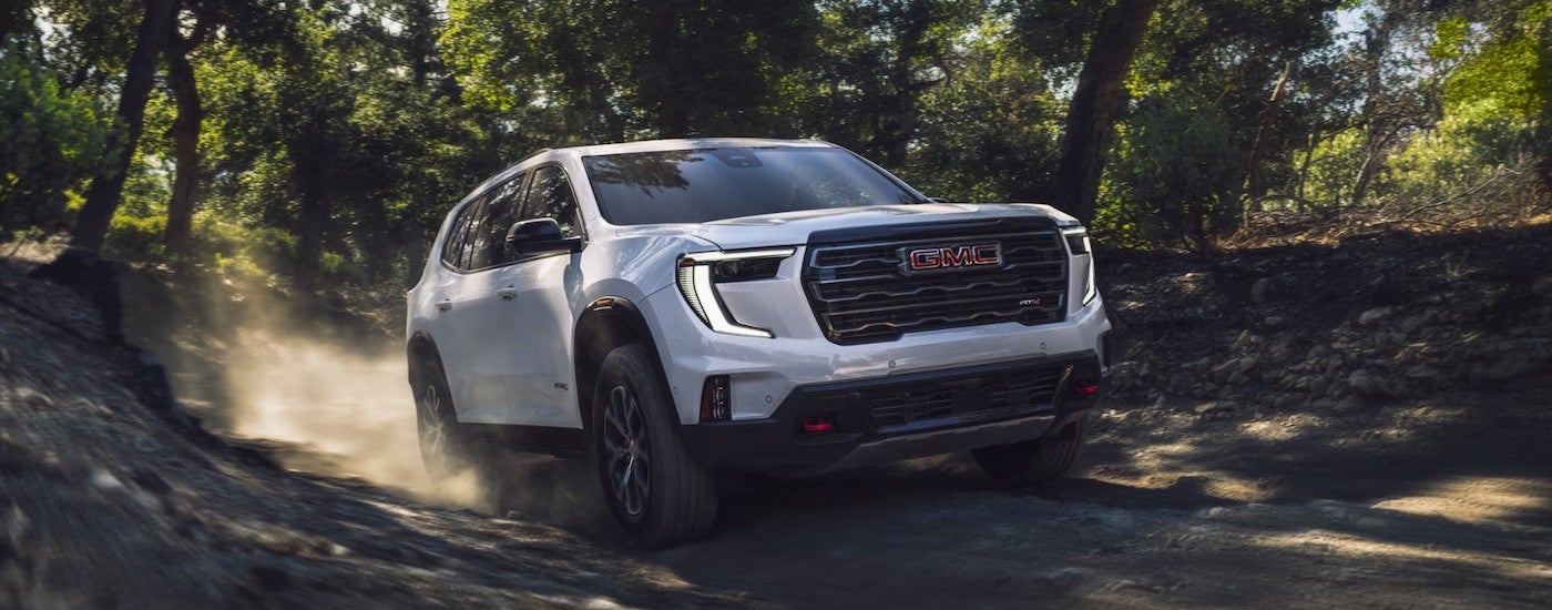 A white 2025 GMC Acadia AT4 from the front while off-road.