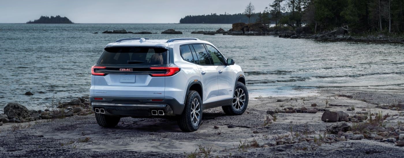 A rear view of a blue 2024 GMC Acadia AT4 parked by a lake.