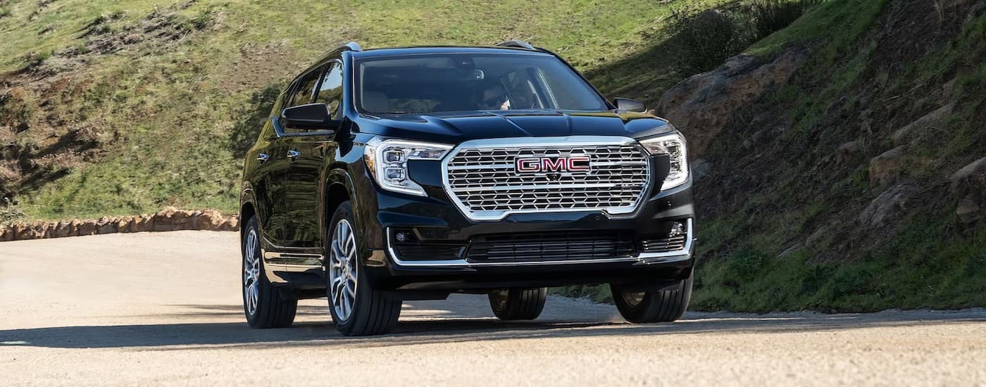 A black 2024 GMC Terrain Denali driving from a GMC dealer near Charlotte.