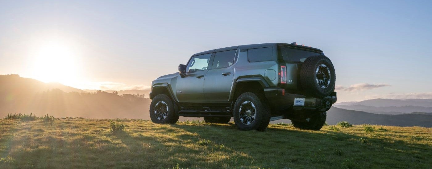 Rear view of a dark green 2024 GMC Hummer EV parked on an open field.