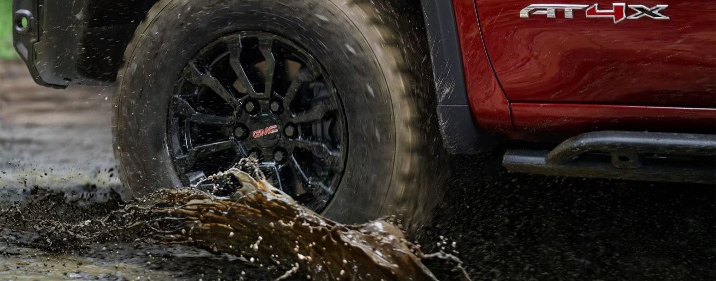 A popular GMC Sierra for sale, a red 2023 GMC Sierra 1500 AT4X, is shown kicking up mud.