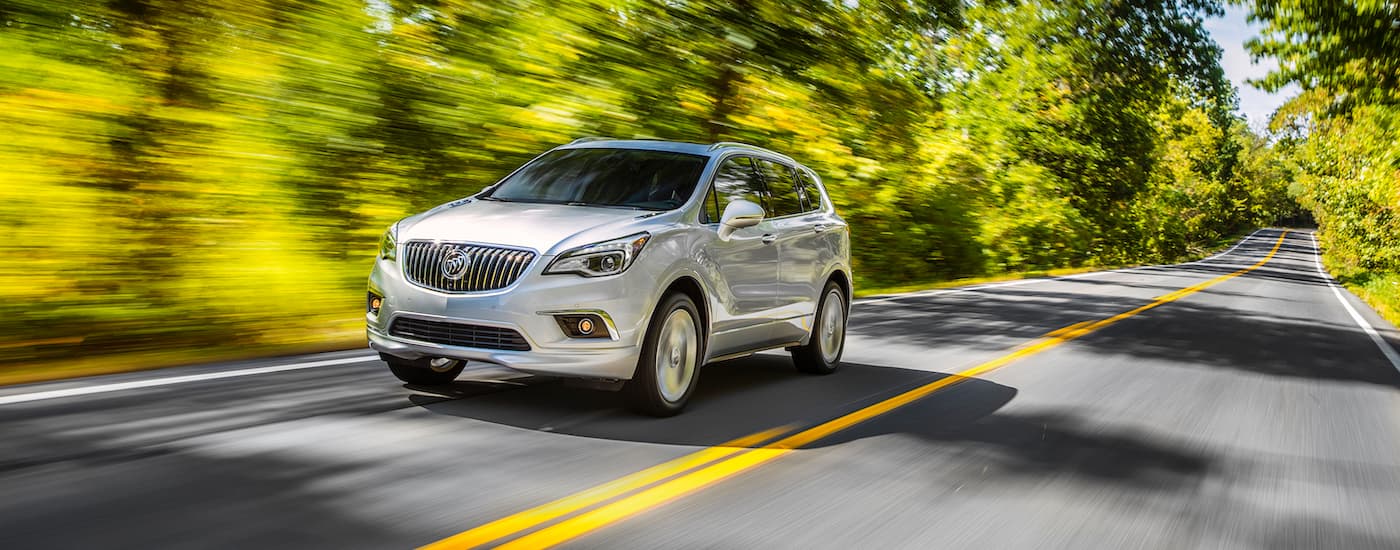 A silver 2017 Buick Envision driving through a forest from a used Buick dealer.