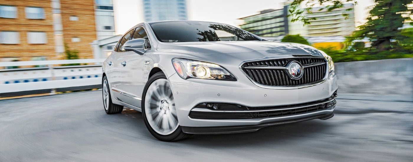 A close-up on the front of a white 2018 Buick LaCrosse driving around a turn.