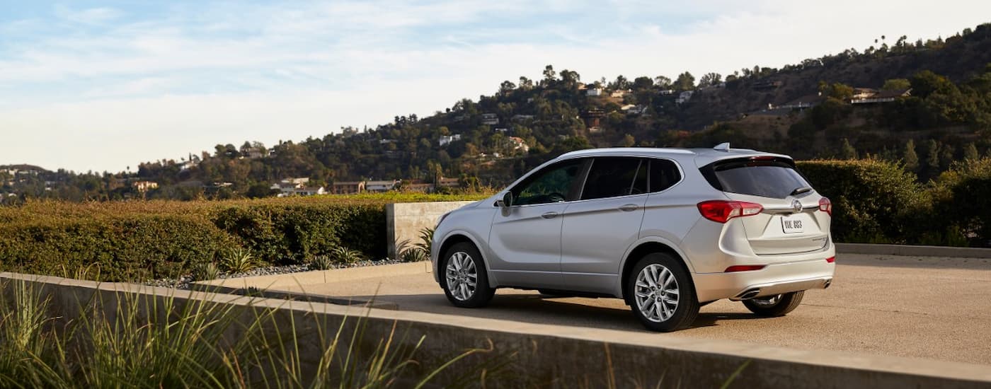 Rear left-angled view of a white 2019 Buick Envision parked in front of a hedge.